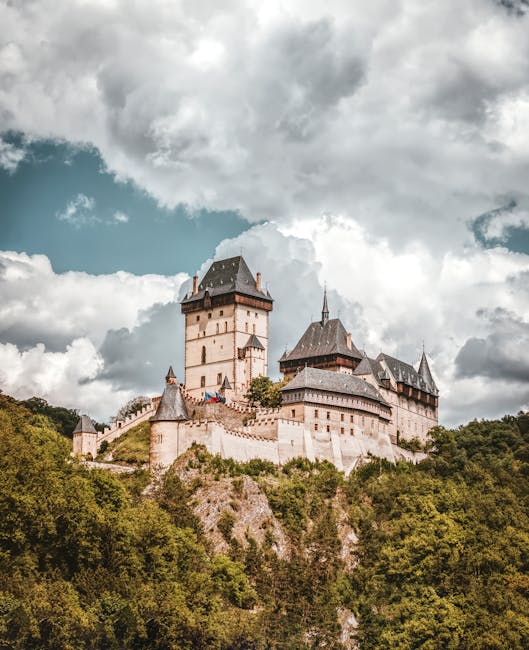A stunning view of a medieval castle on a hilltop surrounded by lush greenery under a dramatic cloudy sky.